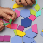 Hands assembling bright color geometric shapes (hexagons and triangles) on a light surface 