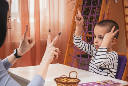 Adult and child at a table using hand signs to communicate 