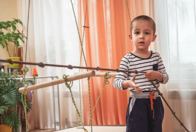 Boy standing at an indoor rope climbing structure, wearing a striped shirt and dark pants, looking at the camera 
