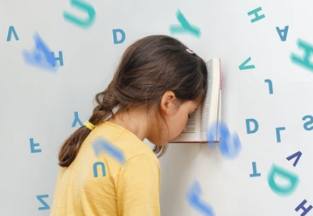 A young girl in a yellow shirt presses an open book to the wall, as colorful letters float around her, suggesting learning or reading themes